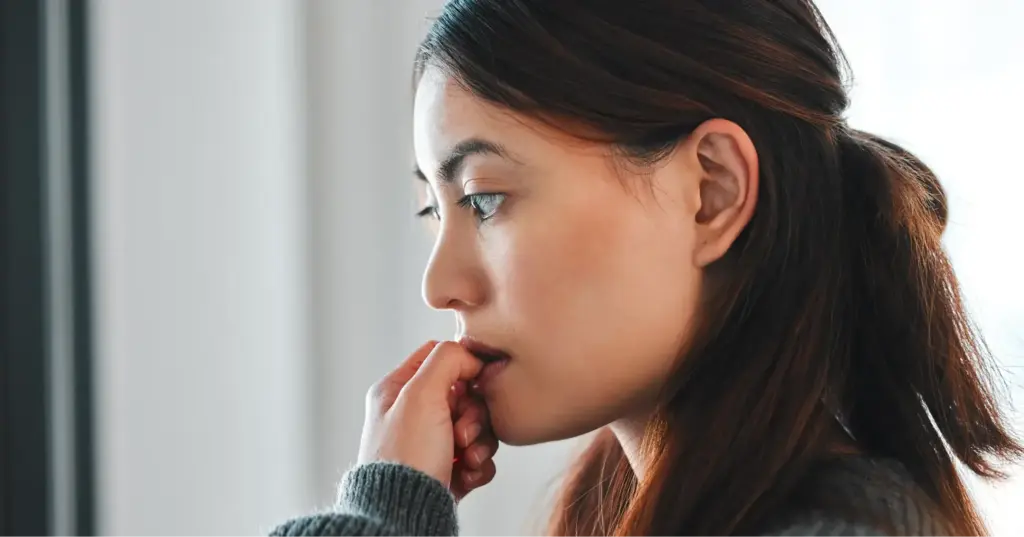 Woman looking anxious and lost in thought while gazing out a window 